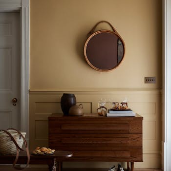 Roomset image featuring wooden chest of drawers and round mirror. Painted in Madeleine, a soft yellow shade. 