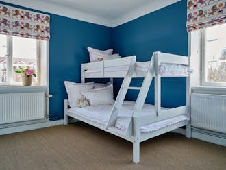 Bedroom with white bunk beds, jute carpet, deep blue (Air Force Blue) walls and two windows with unicorn-themed blinds.