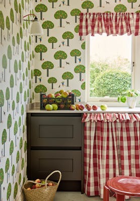 Pantry featuring tree print wallpaper (Rodney Street - Sage & Onions) with dark brown drawers and red gingham hideaway curtain under a window.