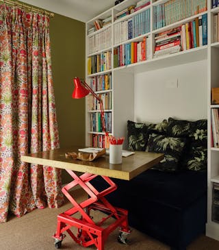 Colorful study with Sir Lutyen’s Sage green left wall with a bright floral curtain and a white right wall with a bookcase.