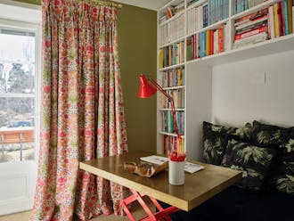 Colorful study with Sir Lutyen’s Sage green left wall with a bright floral curtain and a white right wall with a bookcase.