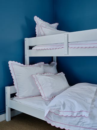 Close-up of white bunk beds featuring white bedding with pink trims in a room with deep blue (Air Force Blue) walls.